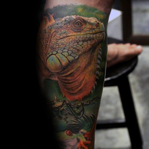 Realistic iguana tattoo in warm orange and green tones, set in a jungle scene with detailed shading and background foliage.