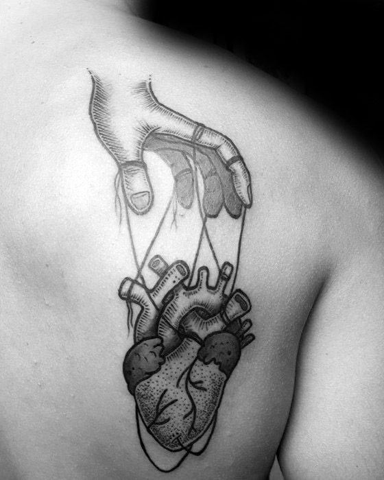 Blackwork puppet tattoo of a hand controlling an anatomical heart with strings, symbolizing emotional manipulation or vulnerability.
