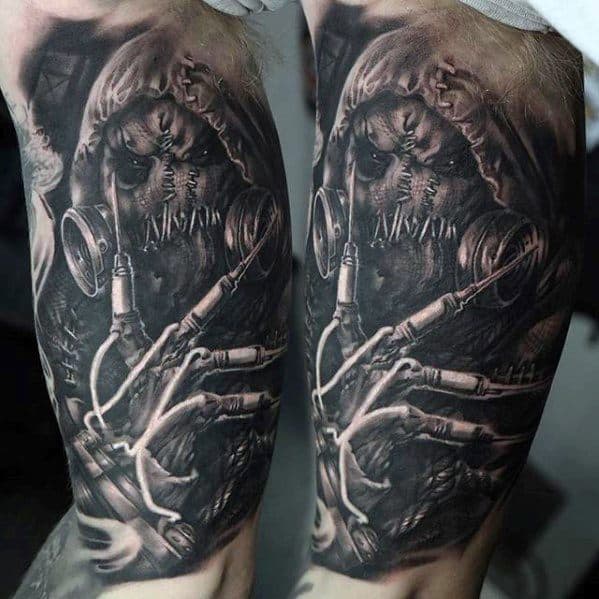 Terrifying scarecrow tattoo with stitched face, gas mask, hood, and detailed hands gripping wires, inked in dark black and grey realism.