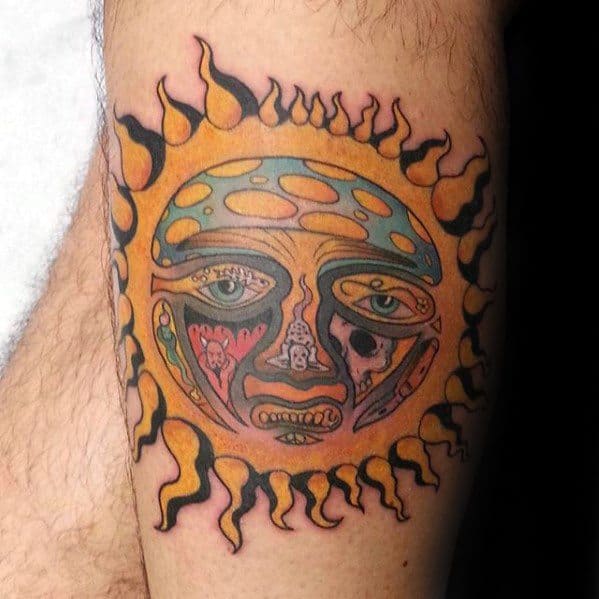 Classic Sublime sun face tattoo on the leg with rich orange, yellow, and green tones, bold flames, and intricate facial details.