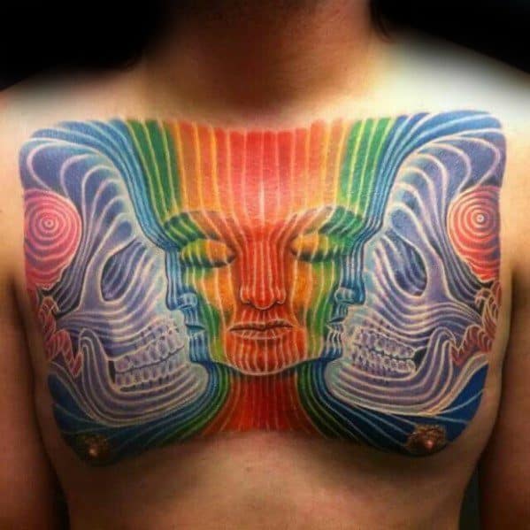 Vibrant Tool-inspired chest tattoo of a meditative central face with mirrored skulls, radiating rainbow lines and psychedelic symmetry.