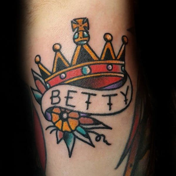 Traditional crown tattoo with bold colors, a flower, and a banner reading “Betty” wrapped around the design.