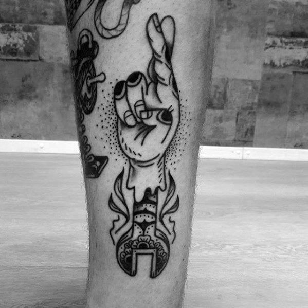 Blackwork tattoo of a stylized hand with crossed fingers emerging from an ornate wrench, blending surreal and traditional design elements.