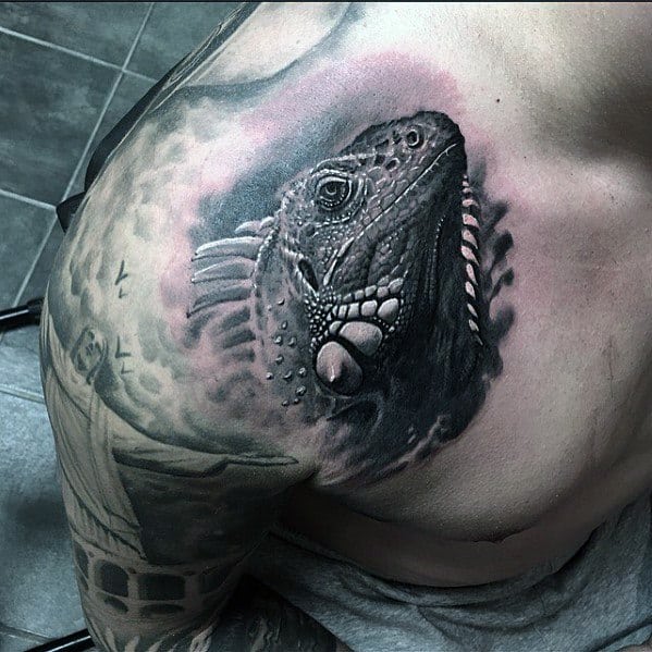 Black and grey iguana tattoo on the chest with high contrast shading, realistic scale detail, and a smoky background effect.