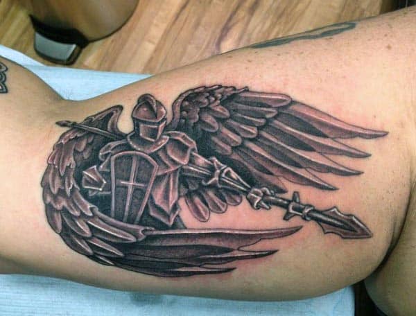Black and grey tattoo of a winged knight in armor holding a spear, featuring bold shading and intricate details on the inner bicep