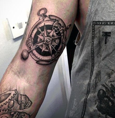 Black and grey tattoo of a detailed compass with intricate gears and shading, creating a mechanical and nautical theme on the inner bicep