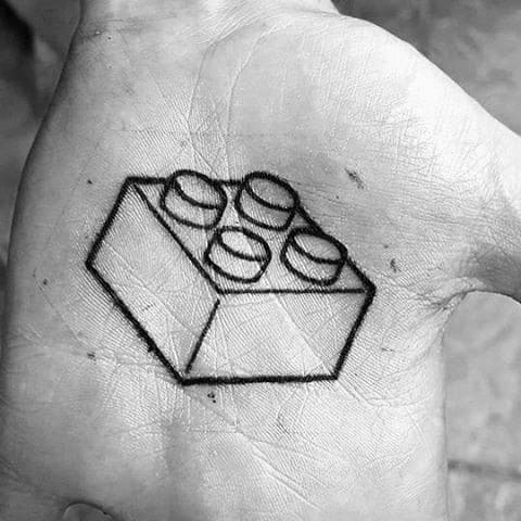 Minimalist black line tattoo of a 3D Lego brick placed on the palm, using clean geometric lines for a bold and simple look.
