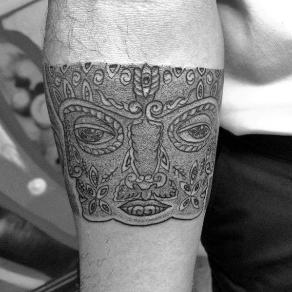 Black and grey Tool-inspired forearm band tattoo featuring a symmetrical face with intricate patterns, swirls, and floral details.