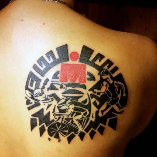 Ironman logo tattoo surrounded by intricate tribal patterns, with the red Ironman symbol in the center and illustrations of swimming, cycling, and running.