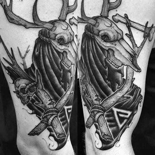 Bold black and grey Witcher tattoo of a Leshen skull with antlers, tattered cloak, runes, and forest elements on the upper arm.