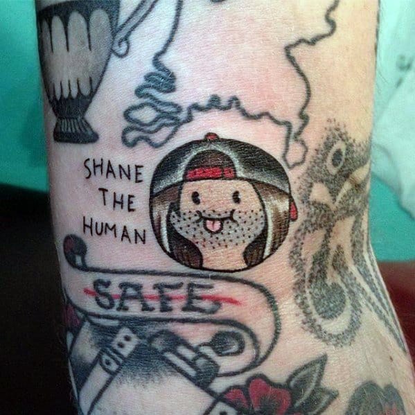 Adventure Time-inspired tattoo of a custom character labeled "Shane the Human" with long hair, a cap, and a tongue out, inked near the wrist.
