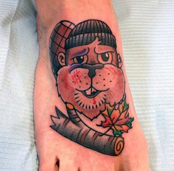 Cartoon beaver tattoo on foot with a beanie, bruised face, maple leaf, and log, giving a tough yet charming expression.