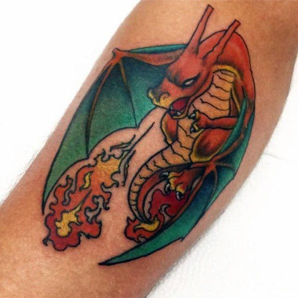 Fierce Charizard tattoo with green wings, vivid orange flames, and a curled pose, combining bold outlines with rich color shading.