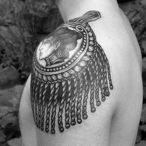 Epaulette tattoo with a classical female profile, beaded frame, and thick rope-like tassels cascading over the upper arm.