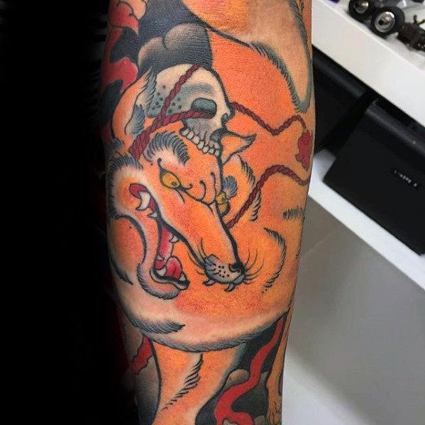 Bold Japanese-style tattoo of a dynamic fox with a skull on its back, vibrant orange tones and flowing black and red accents.