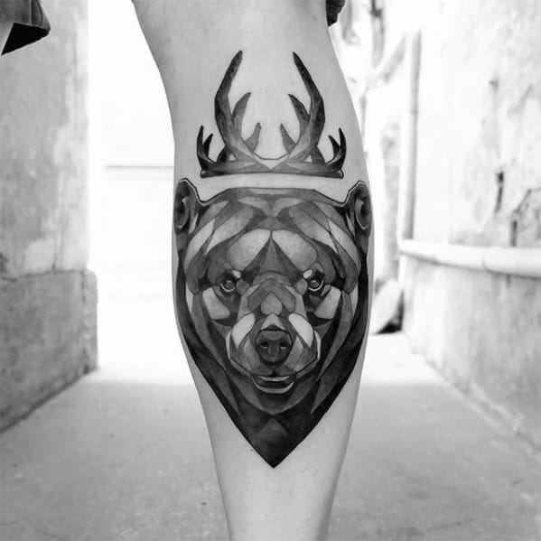 Geometric bear tattoo on the calf with bold shading and sharp facets, featuring a pair of antlers above its head for a unique hybrid design.