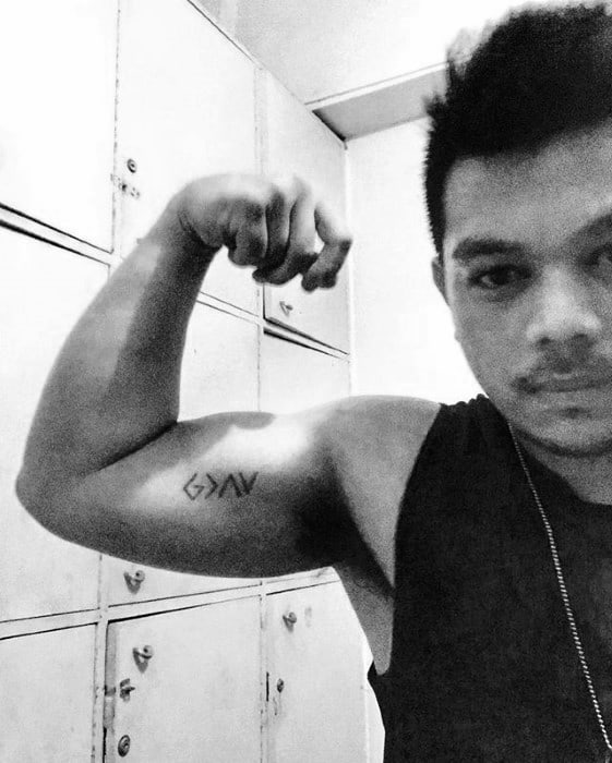Bicep tattoo featuring "God is greater than the highs and lows" symbol in minimalist black line design