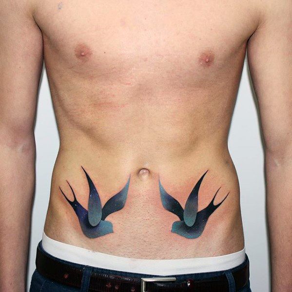 Matching tattoos of two swallows on the lower abdomen with smooth blue-to-black gradients and subtle starry detailing on the wings.