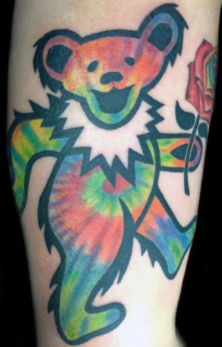 Grateful Dead dancing bear tattoo with vibrant tie-dye colors holding a red rose, outlined in bold black ink.