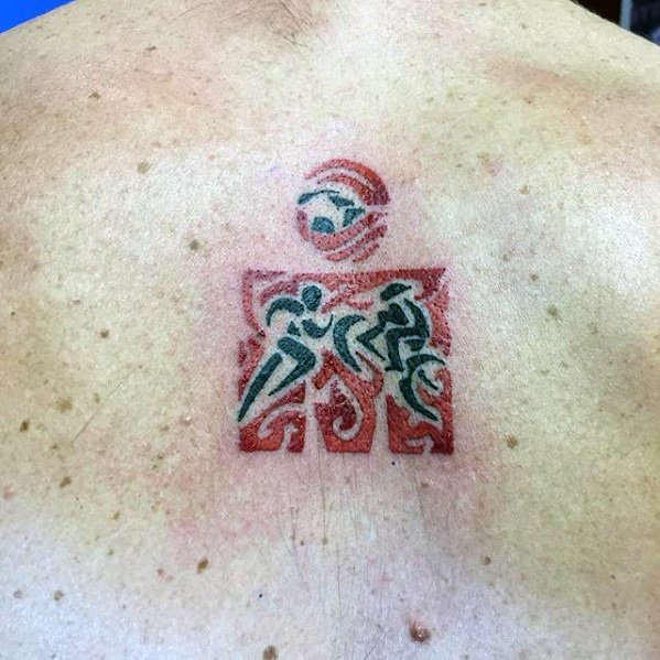 Ironman logo tattoo with a minimalist design, featuring swimmer, cyclist, and runner icons, with a red and green color scheme. The tattoo is framed by intricate patterns.