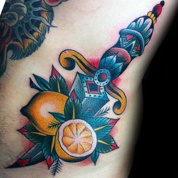 Bold traditional-style tattoo of a dagger piercing through a lemon with surrounding leaves and a lemon slice, featuring rich colors and sharp lines.