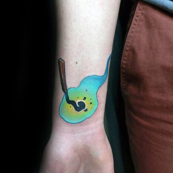 Colorful forearm tattoo of a burnt matchstick with blue and yellow smoke, symbolizing calm after intensity, transformation, and emotional release.