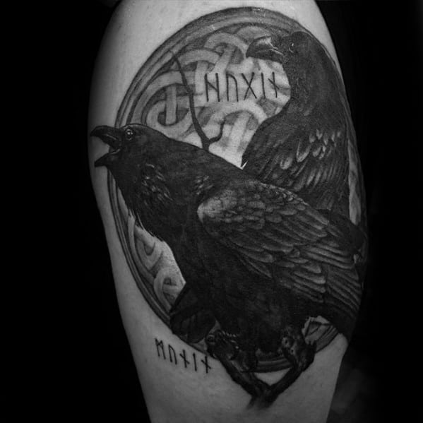 Realistic black and grey tattoo of Huginn and Muninn with runes and a Norse knotwork circle, inked on the upper arm.