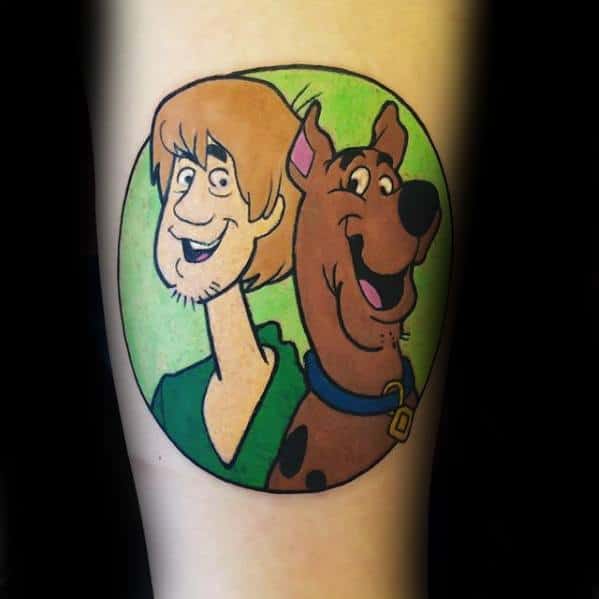 Tattoo of Shaggy and Scooby-Doo smiling inside a green circle, both characters looking cheerful and relaxed.
