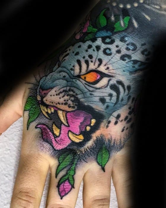Vibrant snow leopard tattoo on the hand with glowing orange eyes, pink tongue, and green leaves for a bold, jungle-inspired look.
