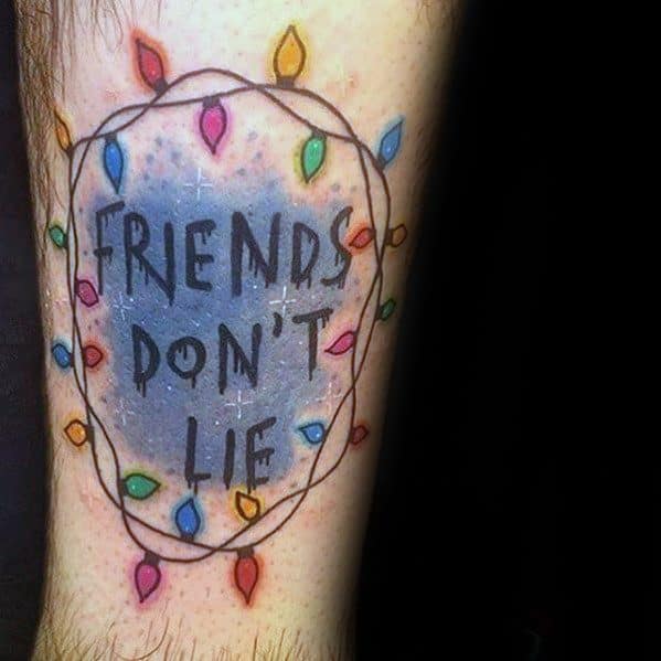 Colorful Stranger Things tattoo of the quote “Friends Don’t Lie” surrounded by a glowing string of Christmas lights.