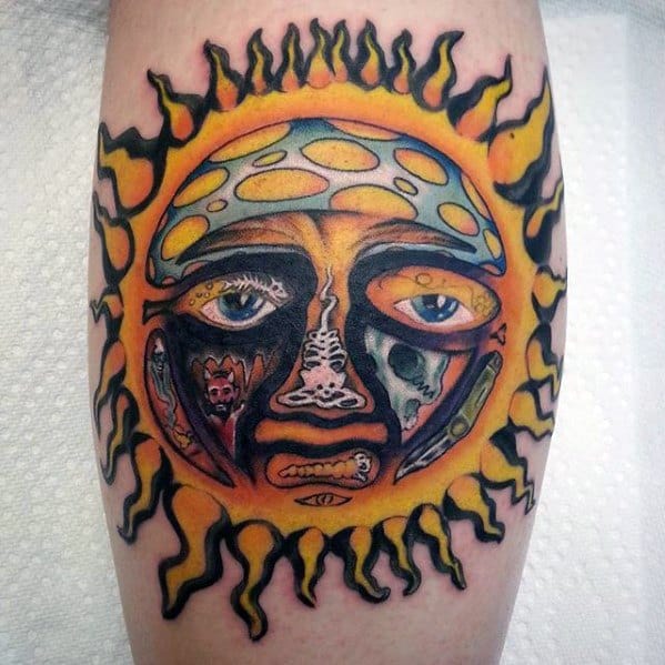 Vibrant Sublime sun face tattoo with intense yellow flames, detailed facial expressions, and contrasting dark and colorful tones on the leg.