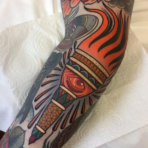 Colorful torch tattoo with a glowing red eye in the center, vivid flames, and intricate geometric patterns along the handle.