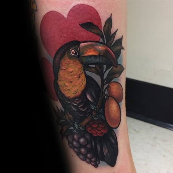 Traditional-style toucan tattoo with fruits, leaves, and a large red heart in the background for a bold and romantic tropical look.