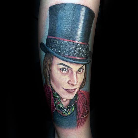Detailed Willy Wonka tattoo inspired by Johnny Depp’s portrayal, with a tall black top hat, red coat, and patterned cravat.
