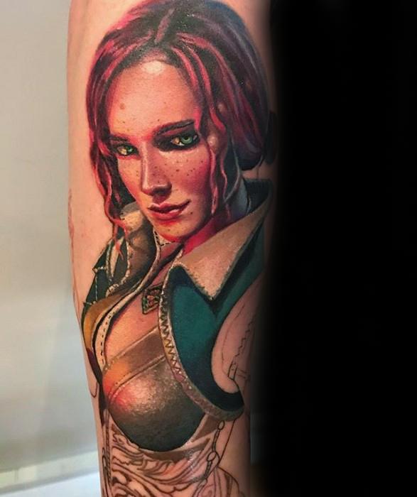 Vivid color tattoo of Triss Merigold from The Witcher, featuring her red hair, green eyes, and detailed outfit on the upper arm.
