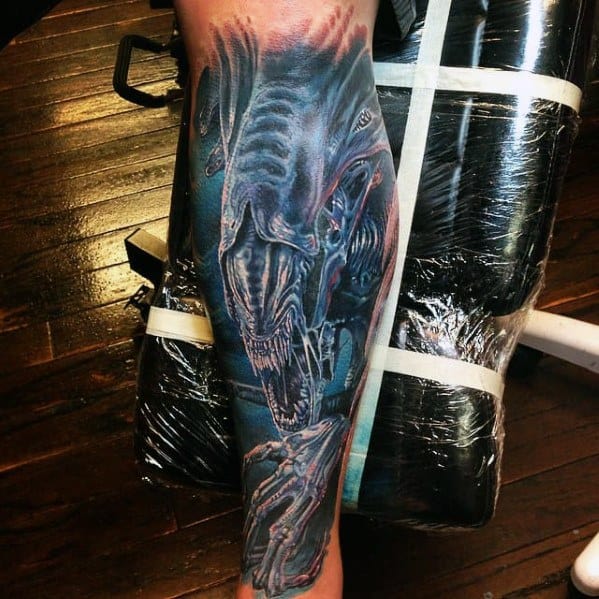 Full-leg Xenomorph tattoo in vivid blue tones with glowing highlights, featuring sharp teeth, claws, and a menacing alien expression.