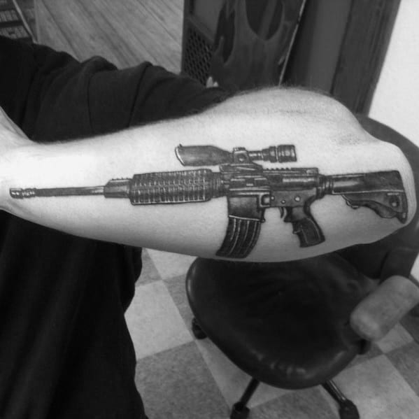 Black and grey AR-15 tattoo on the forearm, featuring a detailed design with a scope and magazine, symbolizing strength and tactical precision.