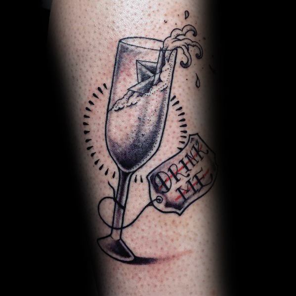 Tattoo of a champagne glass with liquid splashing, labeled "Drink Me," decorated with dynamic lines and shading on skin.