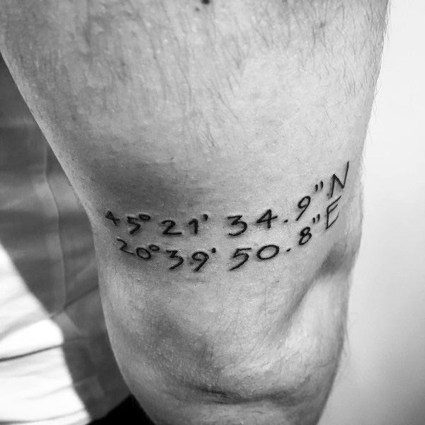 Minimalist coordinate tattoo on the upper arm with clean black lettering, marking a meaningful location with a simple and elegant design.
