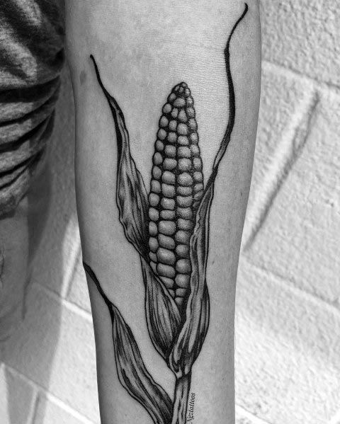 Black and gray tattoo of a detailed corn cob with husks, featuring fine linework and shading for a realistic and elegant design.