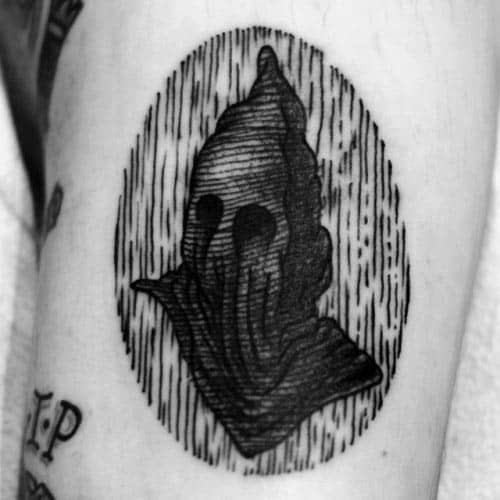 Blackwork executioner tattoo featuring a hooded figure with hollow eyes, detailed with fine line shading inside an oval frame.