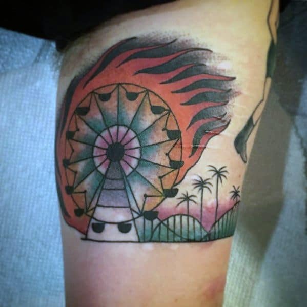 Colorful Ferris wheel tattoo with a bold sunburst design, palm trees, and a roller coaster, creating a vibrant amusement park-inspired scene.