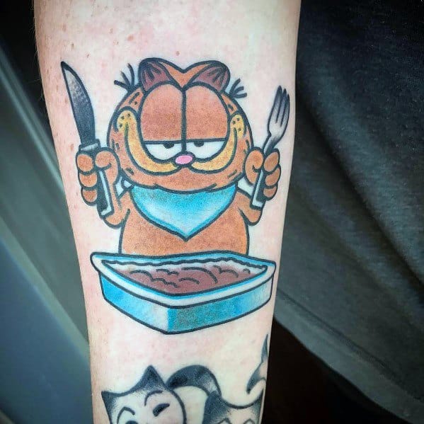 Garfield tattoo holding a knife and fork, ready to eat lasagna—bold colors and a fun design perfect for food and cartoon lovers.