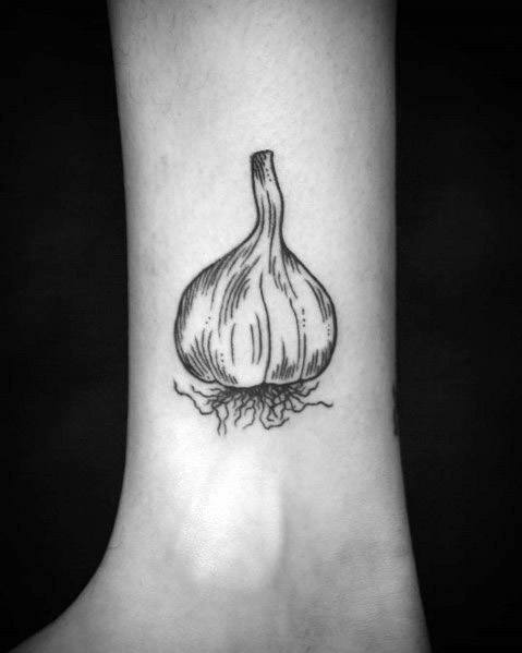 Minimalist black and grey garlic tattoo on the ankle with fine linework and delicate root details, creating a simple yet elegant botanical design.
