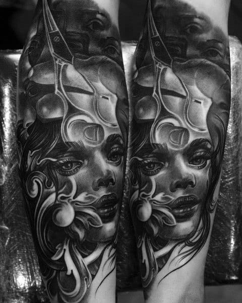 Black and grey forearm tattoo featuring a surreal female face merged with abstract patterns, a mask, and flowing ornamental details for a gothic aesthetic.