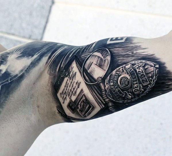 Tattoo featuring a magnifying glass, police badge, and documents, designed with intricate shading for a bold and realistic detective-themed look.