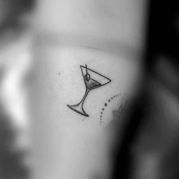 Minimalist martini glass tattoo with a simple black outline and an olive garnish. A small and elegant design with clean, delicate lines.