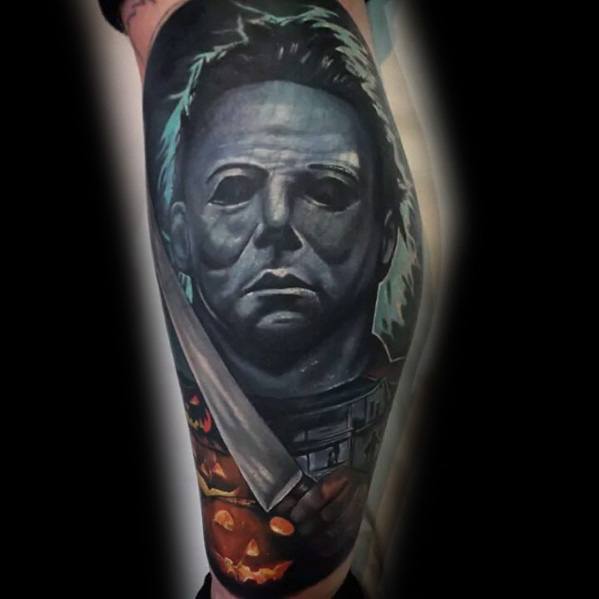 Michael Myers tattoo with a dark, eerie design featuring his iconic mask, a bloodied knife, jack-o'-lanterns, and the infamous house.