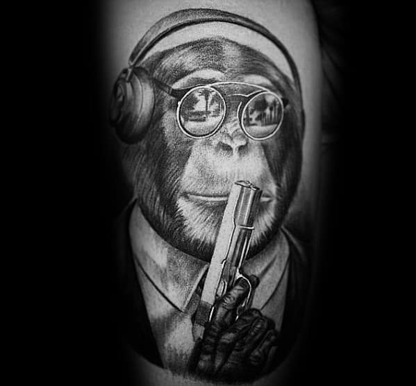 Realistic black and gray tattoo of a chimpanzee wearing headphones and sunglasses, dressed in a suit, holding a 1911 pistol in a bold design.