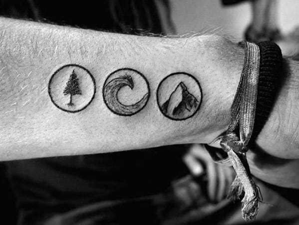 Black ink forearm tattoo featuring three circular symbols: a tree, a wave, and a mountain, representing nature, balance, and adventure.